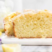 The cross section of a Lemon Olive Oil Loaf Cake showing the most and tender cake topped with a simple sweet lemon glaze on a light background.