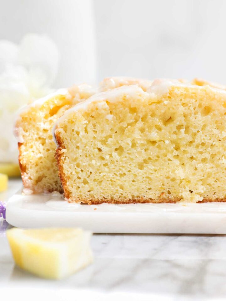 The cross section of a Lemon Olive Oil Loaf Cake showing the most and tender cake topped with a simple sweet lemon glaze on a light background.