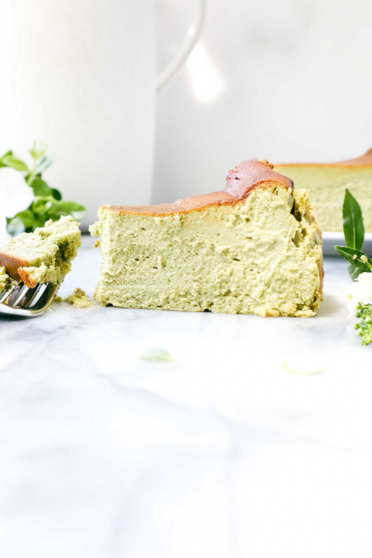 A slice of vibrant green Matcha Basque Cheesecake on white marble background with a fork.