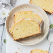 Two slices of Old Fashioned Lemon Pound Cake with lemon glaze on a small dessert plate on a white background.