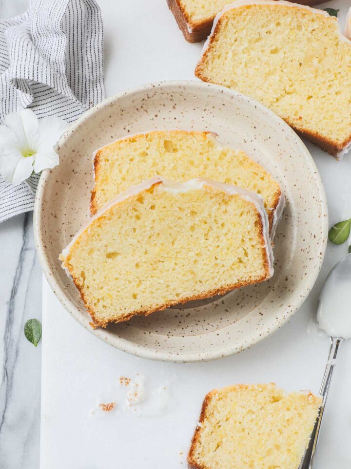Two slices of Old Fashioned Lemon Pound Cake with lemon glaze on a small dessert plate on a white background.