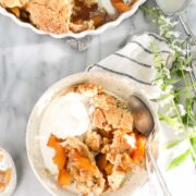 Nectarine Cobbler in a small dessert plate topped with vanilla ice cream with the rest of the cobbler in the background.