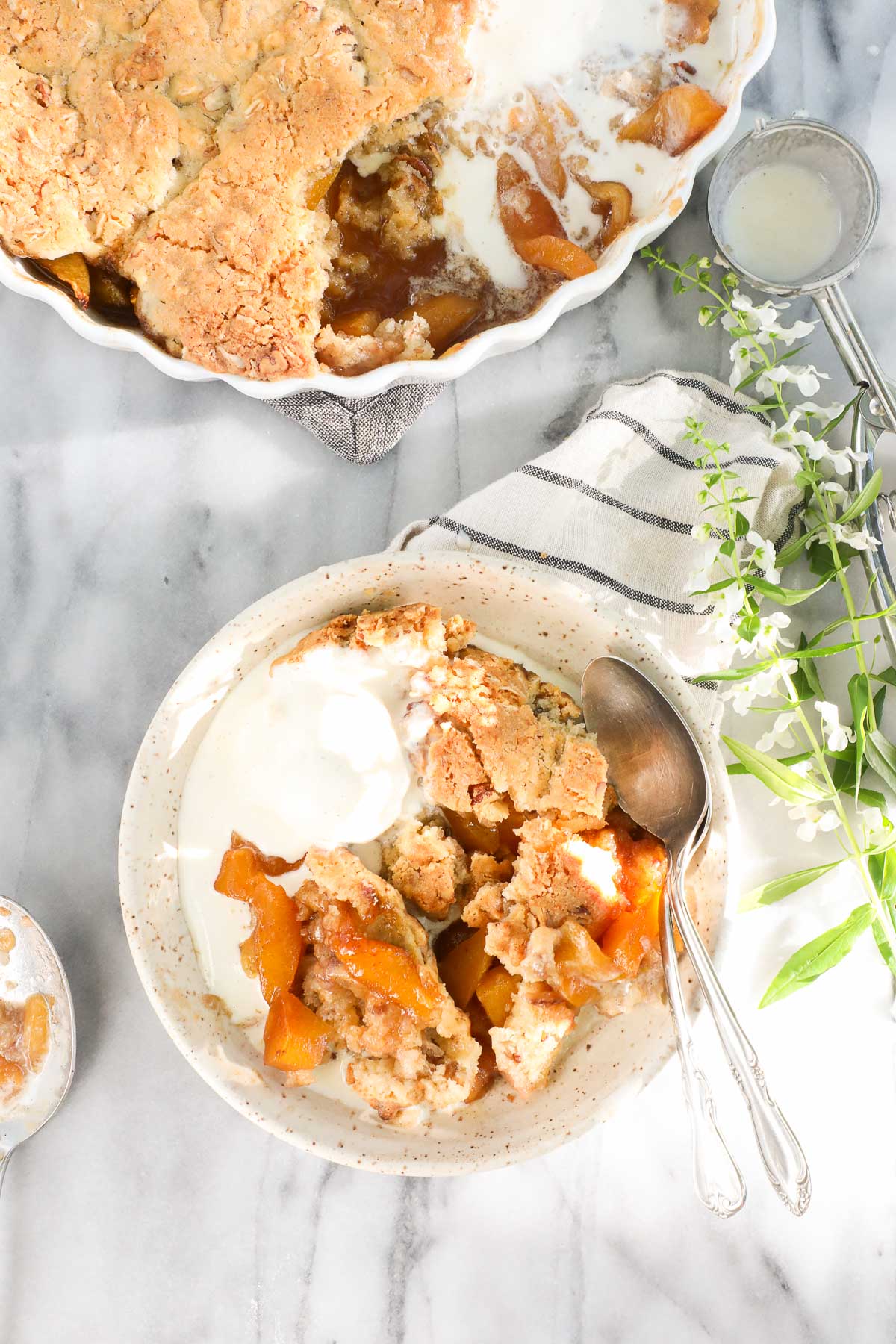 Nectarine Cobbler in a small dessert plate topped with vanilla ice cream with the rest of the cobbler in the background.