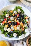 Summer Kale Salad in a bowl with diced nectarines, blueberries, feta, and pumpkin seeds with a tangerine vinaigrette.