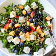 Summer Kale Salad in a bowl with diced nectarines, blueberries, feta, and pumpkin seeds with a tangerine vinaigrette.