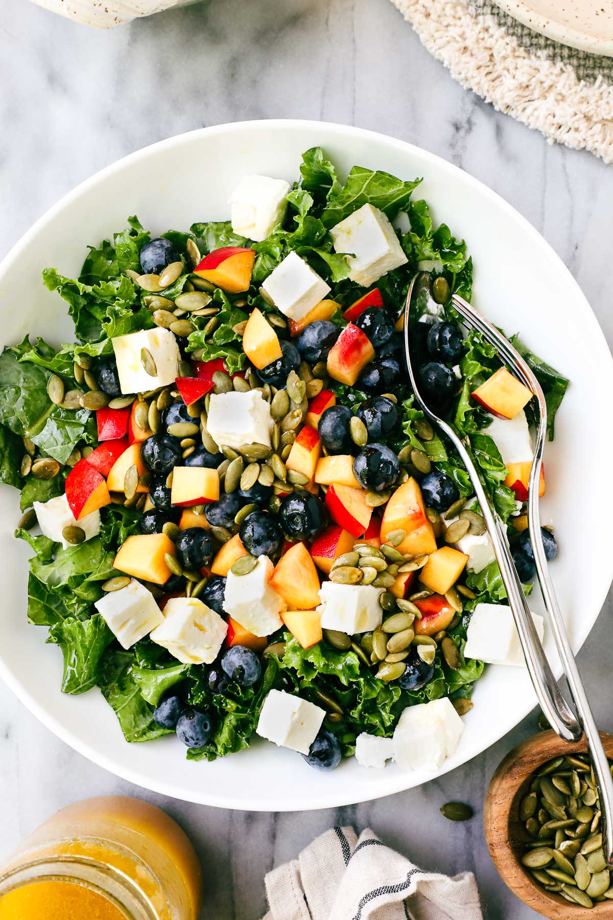 Summer Kale Salad in a bowl with diced nectarines, blueberries, feta, and pumpkin seeds with a tangerine vinaigrette.