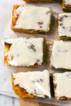 Sweet Cinnamon Roll Pumpkin Focaccia cut into large squares with cream cheese frosting dappled with golden light on a simple light background.
