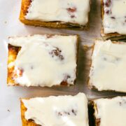 Sweet Cinnamon Roll Pumpkin Focaccia cut into large squares with cream cheese frosting dappled with golden light on a simple light background.