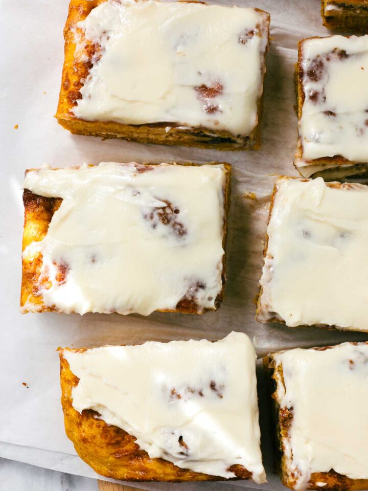 Sweet Cinnamon Roll Pumpkin Focaccia cut into large squares with cream cheese frosting dappled with golden light on a simple light background.