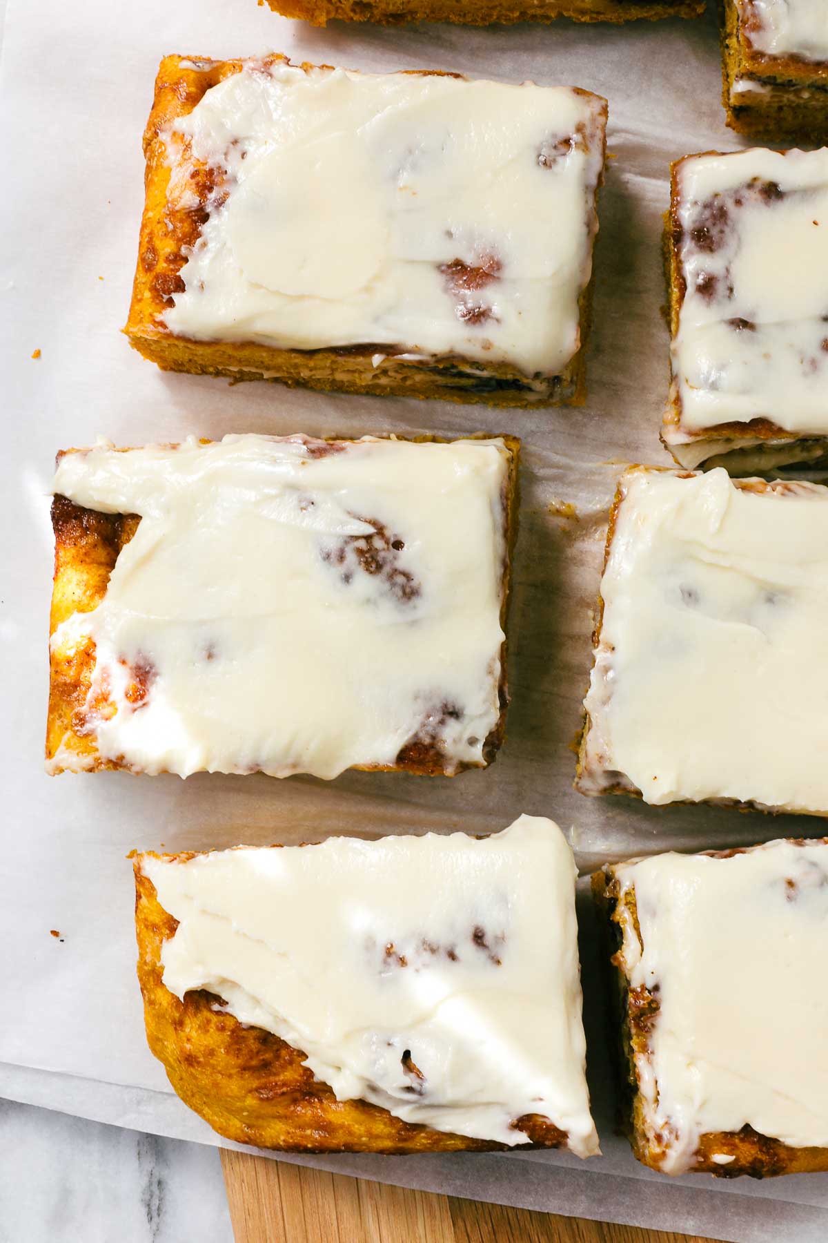 Sweet Cinnamon Roll Pumpkin Focaccia cut into large squares with cream cheese frosting dappled with golden light on a simple light background.