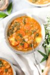 Tuscan White Bean Soup that is vibrant orange in color with cannellini beans, orange carrots, and green kale in a bowl on a soft cream colored napkin.