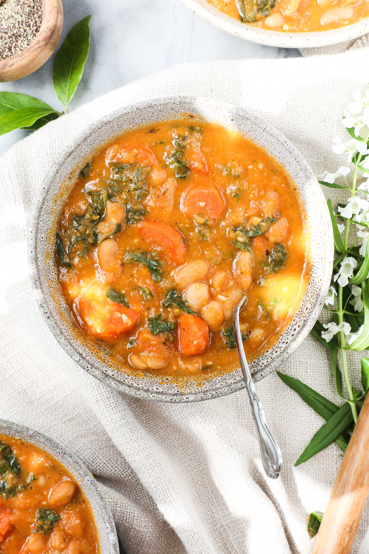 Tuscan White Bean Soup that is vibrant in color with cannellini beans, orange carrots, and green kale in a bowl on a soft cream colored napkin.