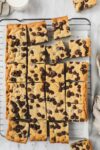 Chocolate Chip Cookie Bars removed from a 9x13 pan and cut into 24 squares laying flat on parchment paper on a cookie drying rack.
