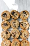Twelve Cookies arranged in four rows of three on a rectangular cookie drying rack on a white marble surface dappled with natural light.