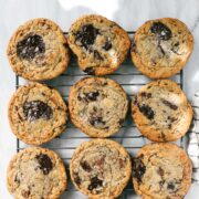 Twelve Cookies arranged in four rows of three on a rectangular cookie drying rack on a white marble surface dappled with natural light.