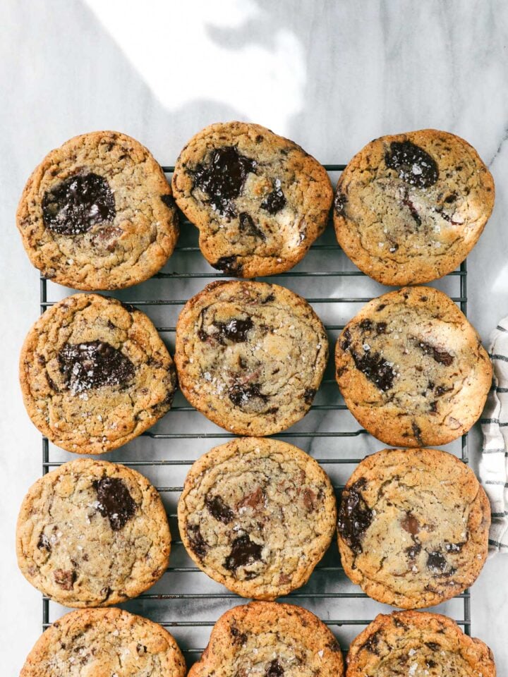 Twelve Cookies arranged in four rows of three on a rectangular cookie drying rack on a white marble surface dappled with natural light.