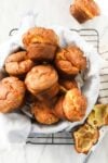 Popovers in a bread basket lined with a soft linen napkin on top of a drying rack on a white marble background.