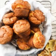 Popovers in a bread basket lined with a soft linen napkin on top of a drying rack on a white marble background.
