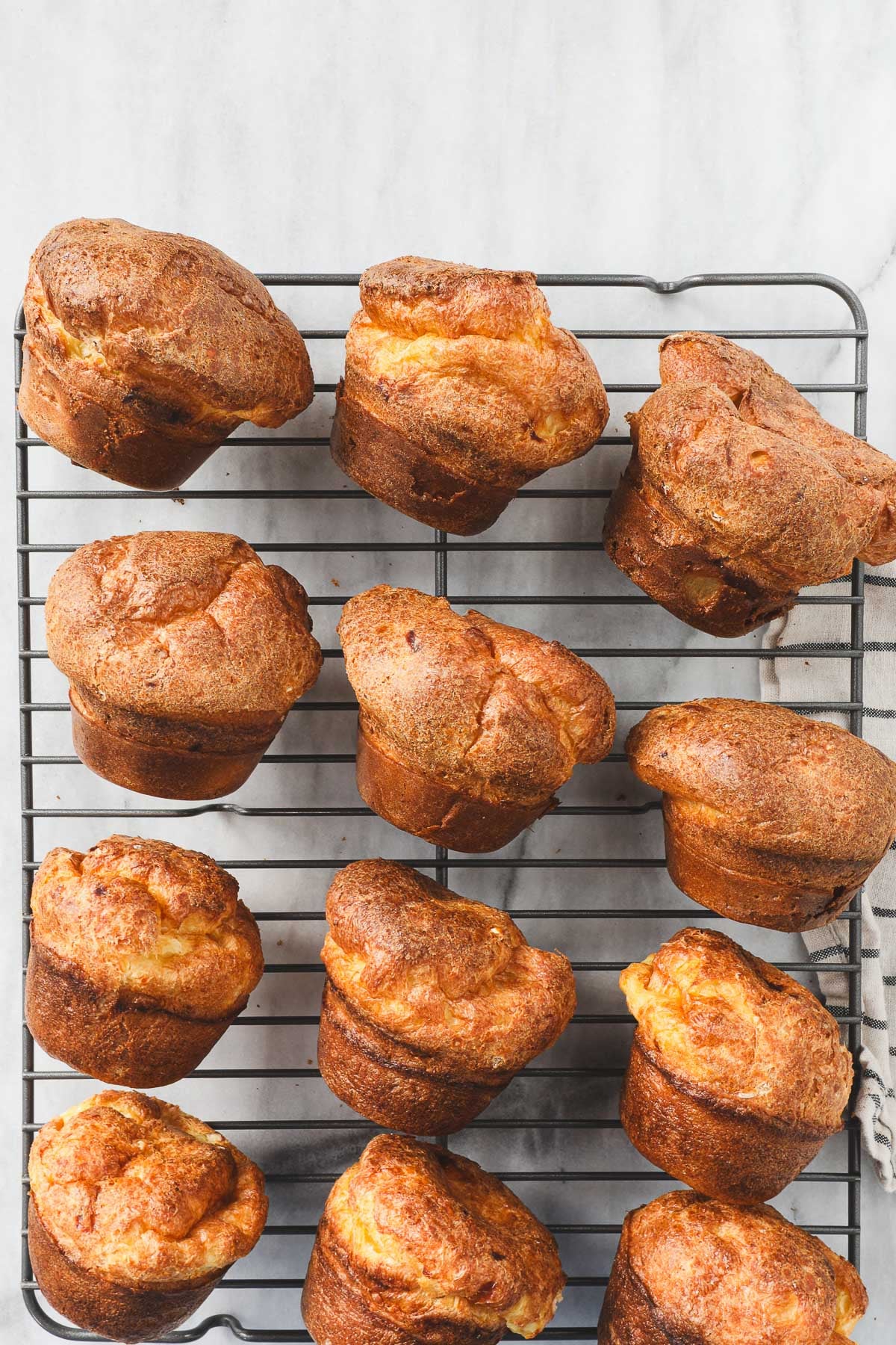 A dozen popovers laying on their sides on a diaganol on a metal drying rack.