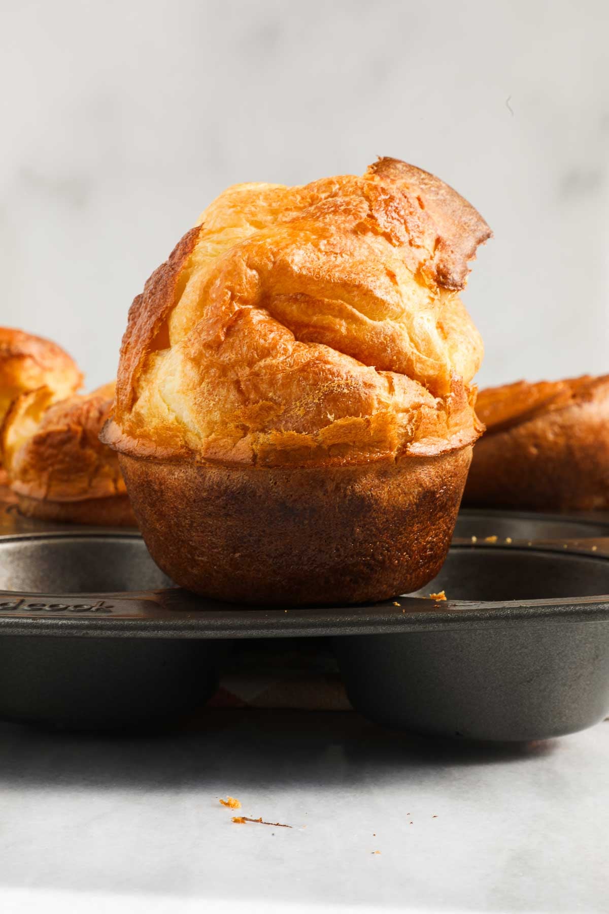 One popover sitting on top of a muffin tin, showing its height.
