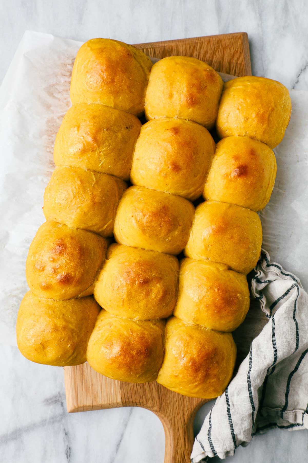 Pumpkin Dinner Rolls in five rows of three on a wooden serving board.