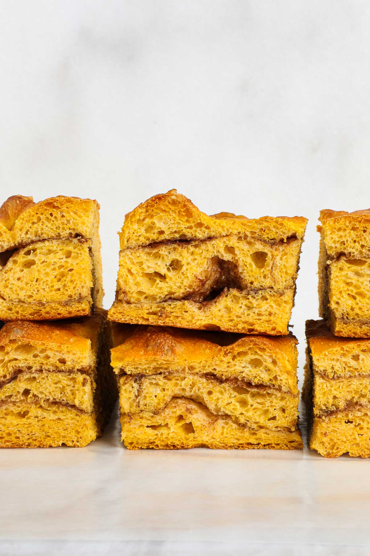 Six slices of Sweet Pumpkin Focaccia stacked in sets of two showing the cinnamon sugar swirl and soft interior of the bread.